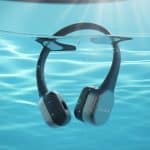 Fones de ouvido para natação submersos em uma piscina azul com bolhas e reflexos de luz na água.