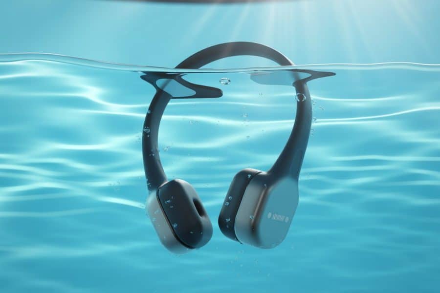 Fones de ouvido para natação submersos em uma piscina azul com bolhas e reflexos de luz na água.
