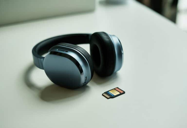 Fone de ouvido moderno preto com acabamento metálico ao lado de um cartão de memória microSD sobre uma superfície branca.