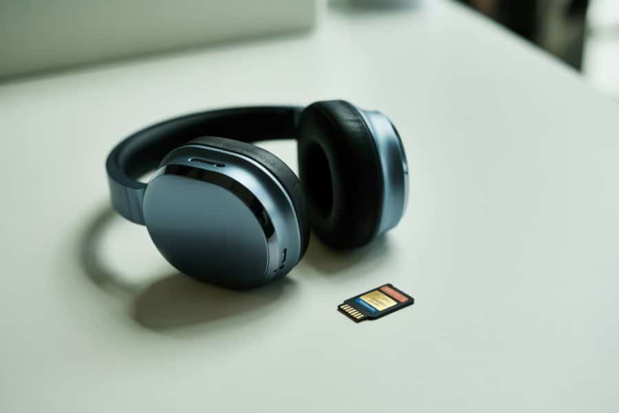 Fone de ouvido moderno preto com acabamento metálico ao lado de um cartão de memória microSD sobre uma superfície branca.