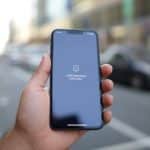 Pessoa segurando um smartphone com um ícone indicando problema de rede na tela, em um fundo urbano desfocado.