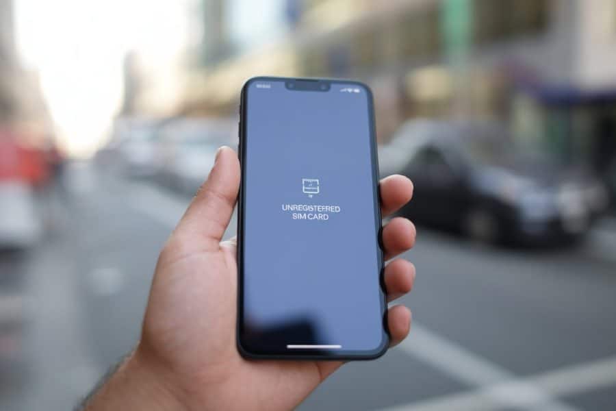 Pessoa segurando um smartphone com um ícone indicando problema de rede na tela, em um fundo urbano desfocado.