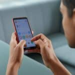 Pessoa segurando um smartphone vermelho Redmi e usando a tela sensível ao toque.