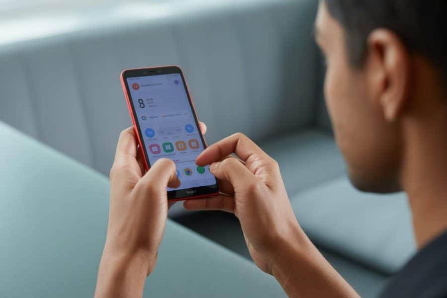 Pessoa segurando um smartphone vermelho Redmi e usando a tela sensível ao toque.
