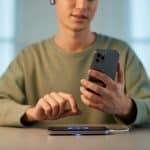 Pessoa usando fone de ouvido Bluetooth enquanto o celular está carregando em uma base sem fio.