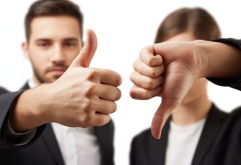 Duas mãos, uma fazendo sinal de positivo com o polegar para cima e outra fazendo sinal de negativo com o polegar para baixo, em fundo neutro e desfocado.