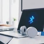 Um laptop moderno sobre uma mesa limpa com fones de ouvido Bluetooth ao lado, mostrando a conexão ativa entre eles.