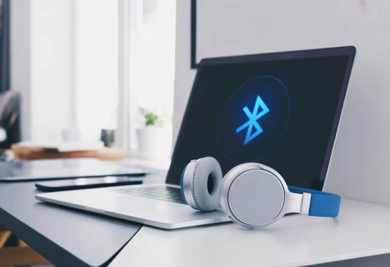 Um laptop moderno sobre uma mesa limpa com fones de ouvido Bluetooth ao lado, mostrando a conexão ativa entre eles.