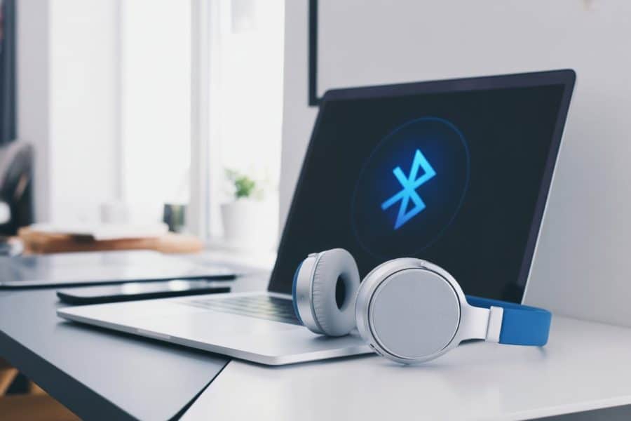 Um laptop moderno sobre uma mesa limpa com fones de ouvido Bluetooth ao lado, mostrando a conexão ativa entre eles.