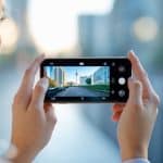 Pessoa segurando um smartphone mostrando a cena vista pela câmera, com fundo desfocado.